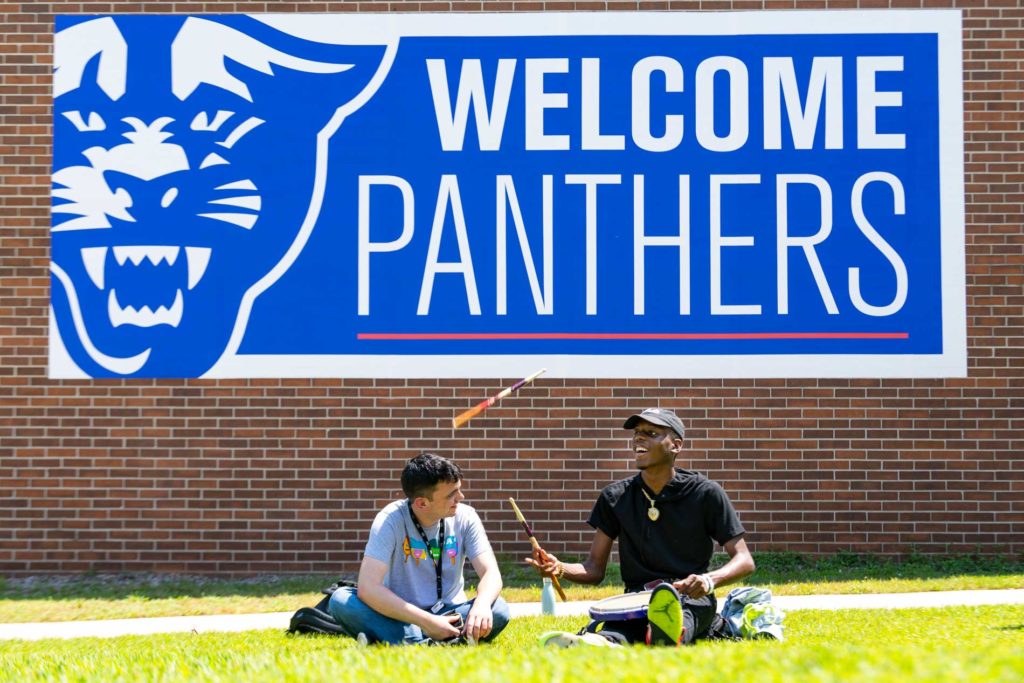Students conversing on campus in front of the Welcome Panthers sign