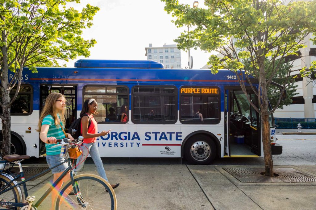 Students walking with bikes, with GSU bus in the background .
